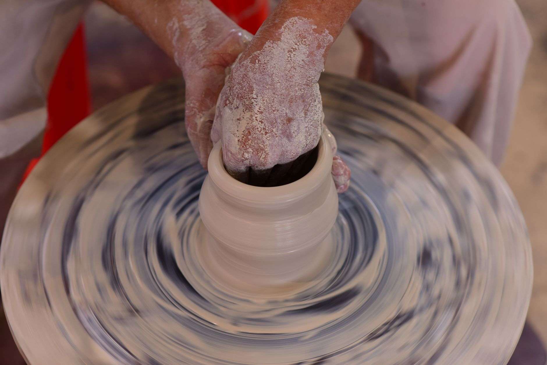 Hands shaping wet clay on a spinning pottery wheel