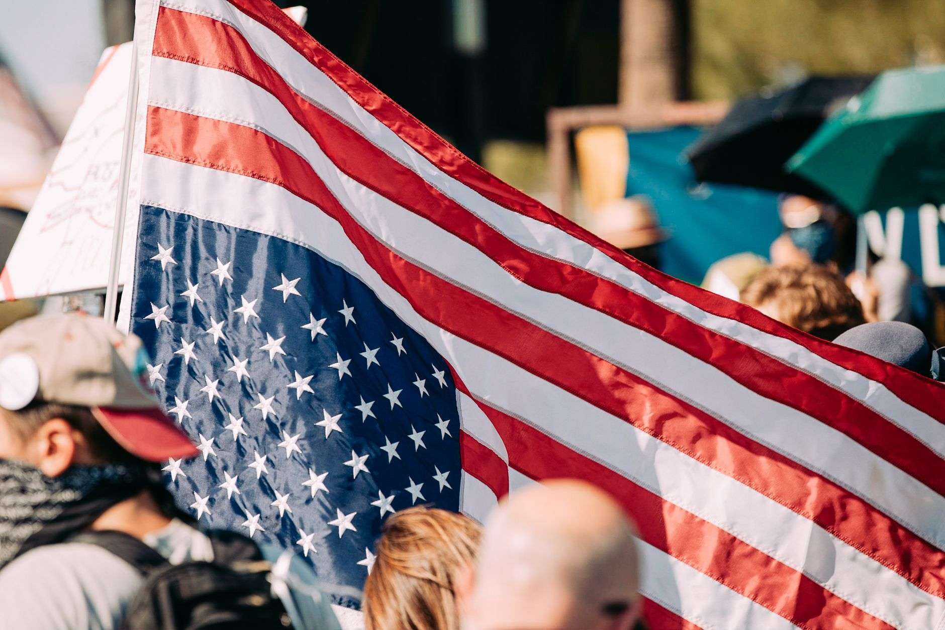 A large American flag waving above a crowd at an outdoor public gathering