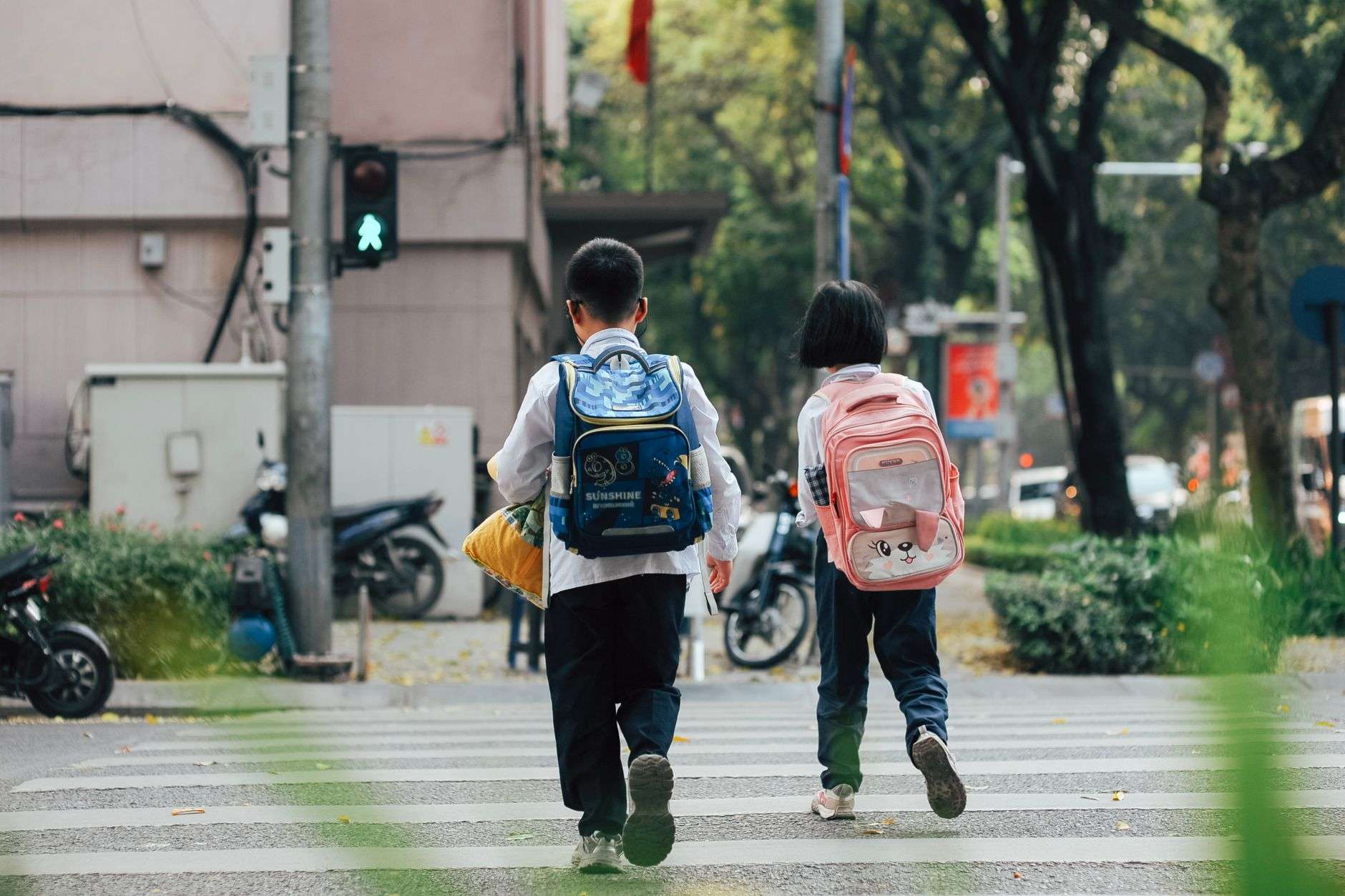 Children with backpacks walking along a sidewalk