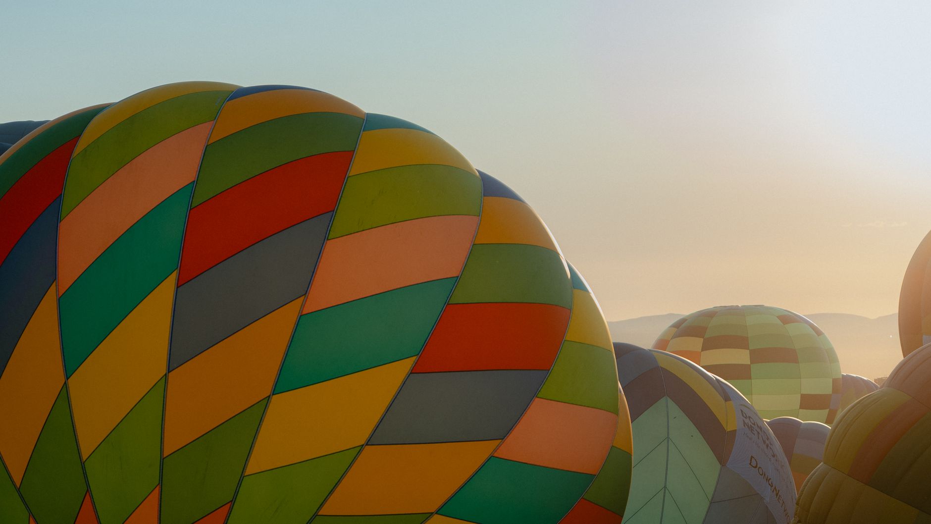 Colorful hot air balloons lift off into a pale morning sky