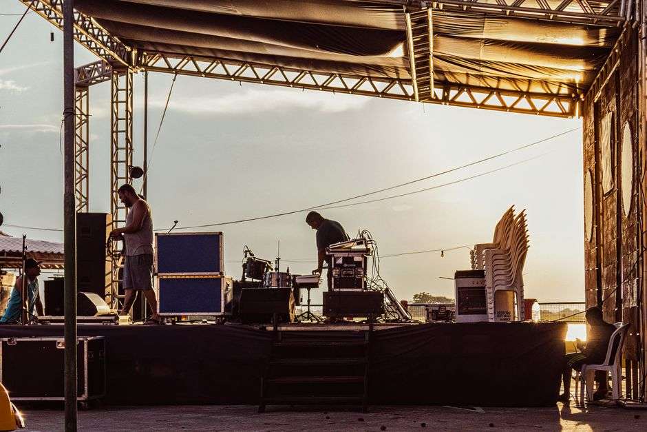 An open-air beach bar with a live music stage facing the water at sunset