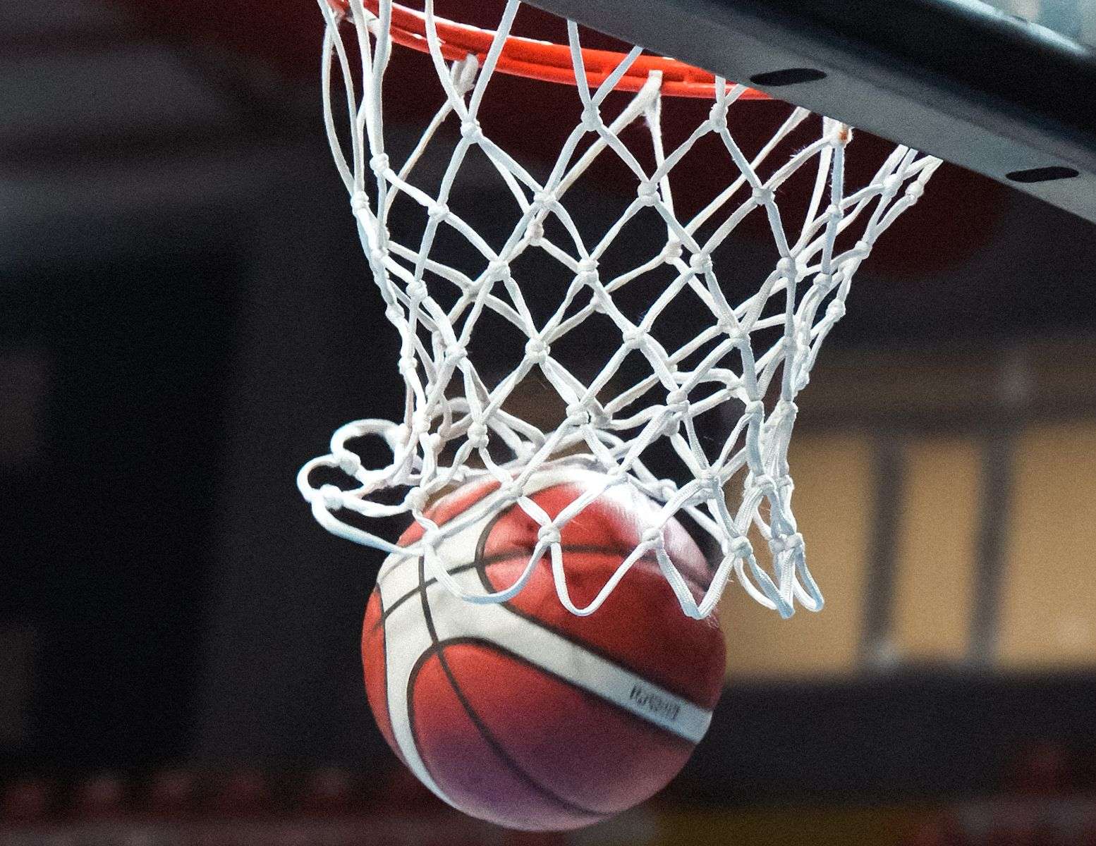 Basketball dropping through a hoop and net, with rows of empty arena seating blurred in the background