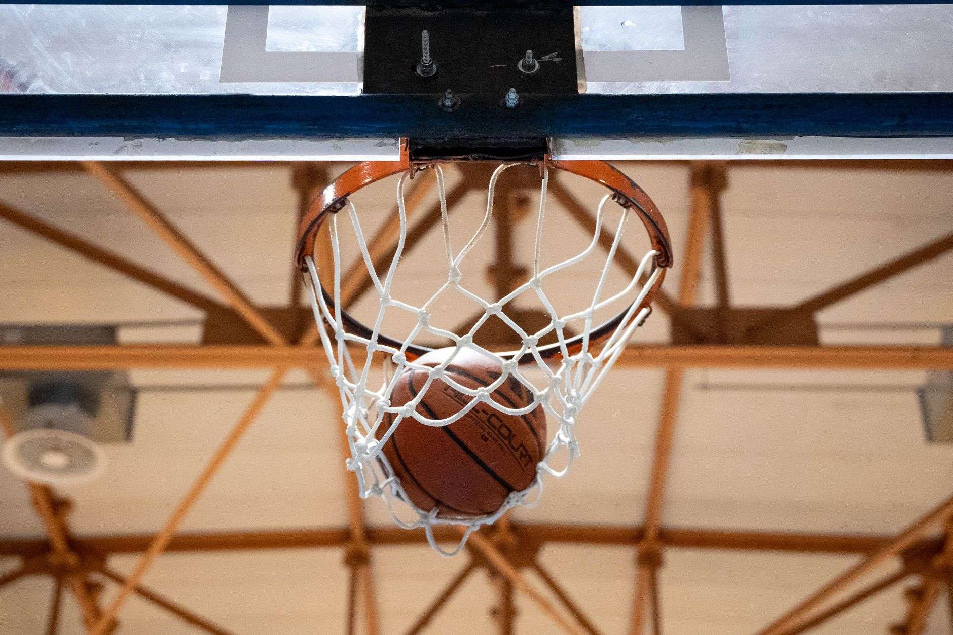 An empty high school basketball gymnasium with a hoop and bleachers