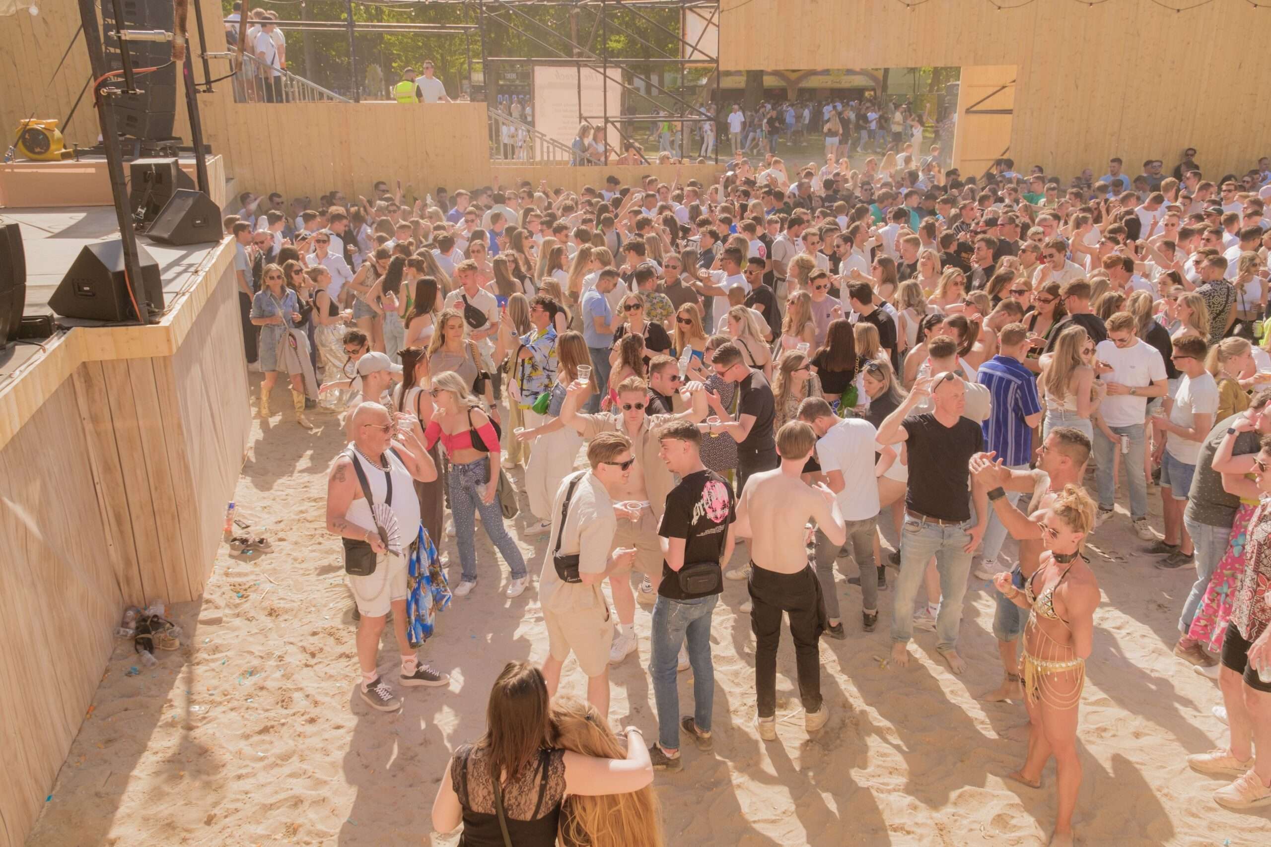 Large crowd gathered on sand in front of an outdoor festival stage on a sunny day