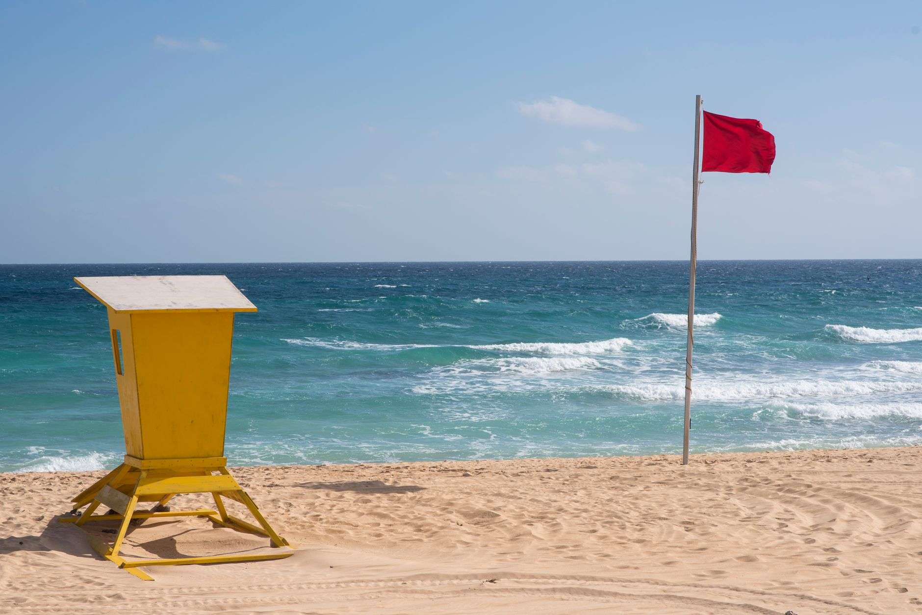 Red warning flag and lifeguard stand on a sandy beach with rough surf
