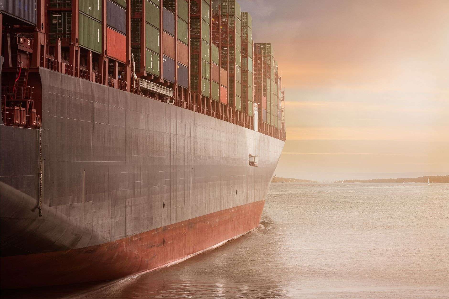 Large container ship loaded with cargo containers on calm water at sunset