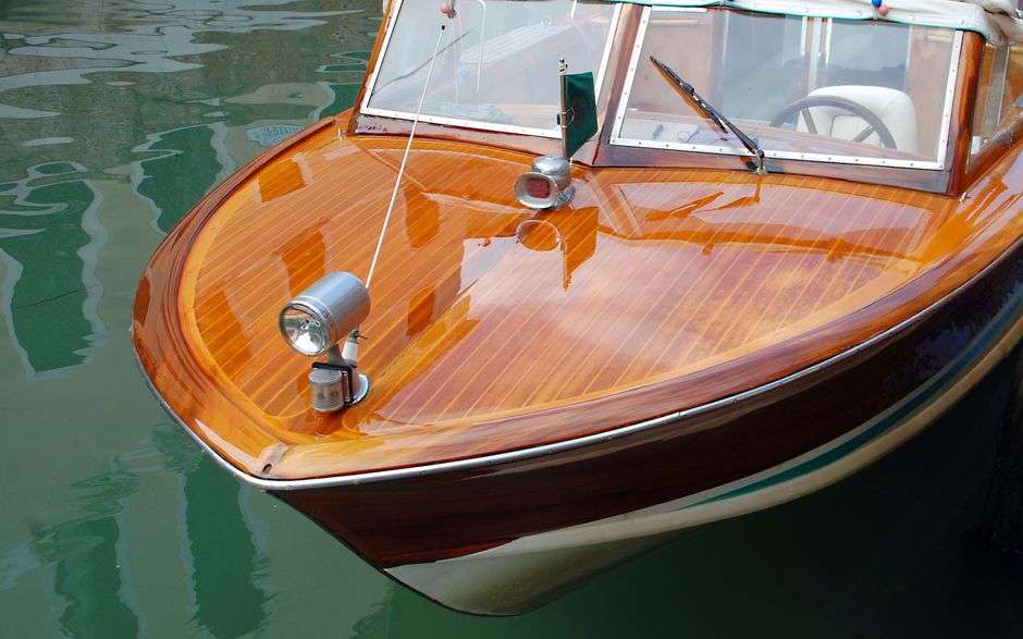 A classic runabout boat with a sweeping bow cruising on calm coastal water