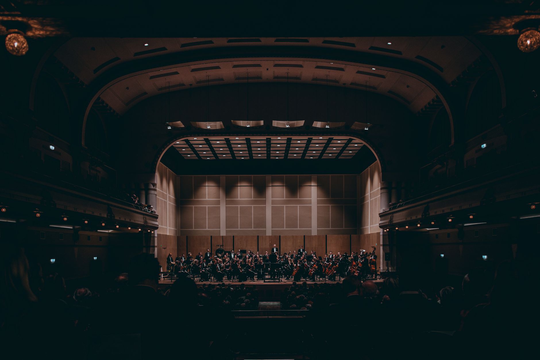 An orchestra performs on stage in a warmly lit concert hall