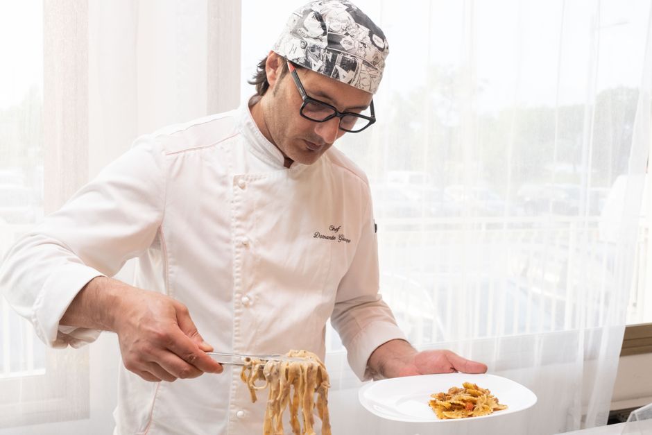 Chef carefully plating a handmade pasta dish in a professional restaurant kitchen