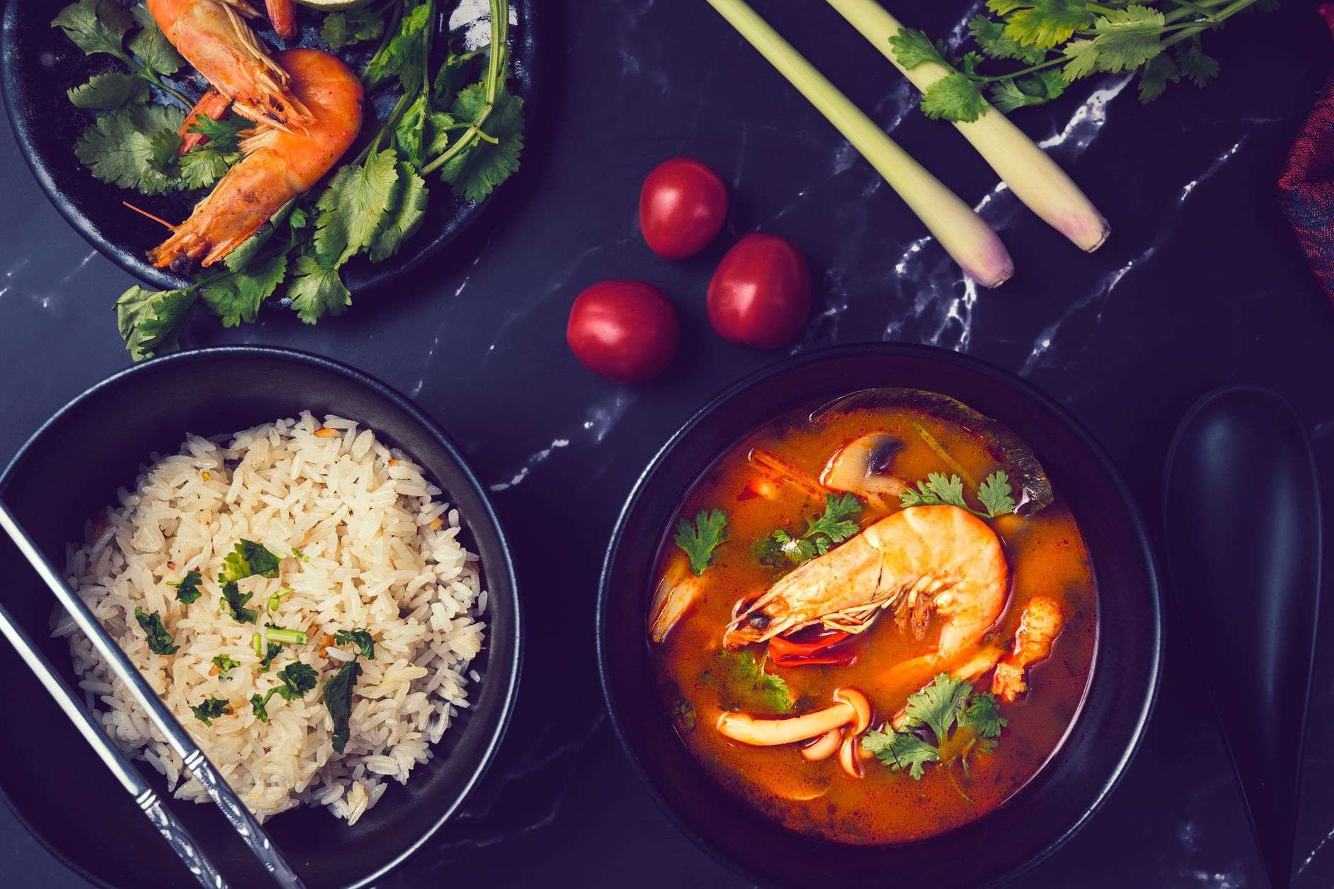 A dark bowl of seafood gumbo with shrimp and white rice on a wooden table
