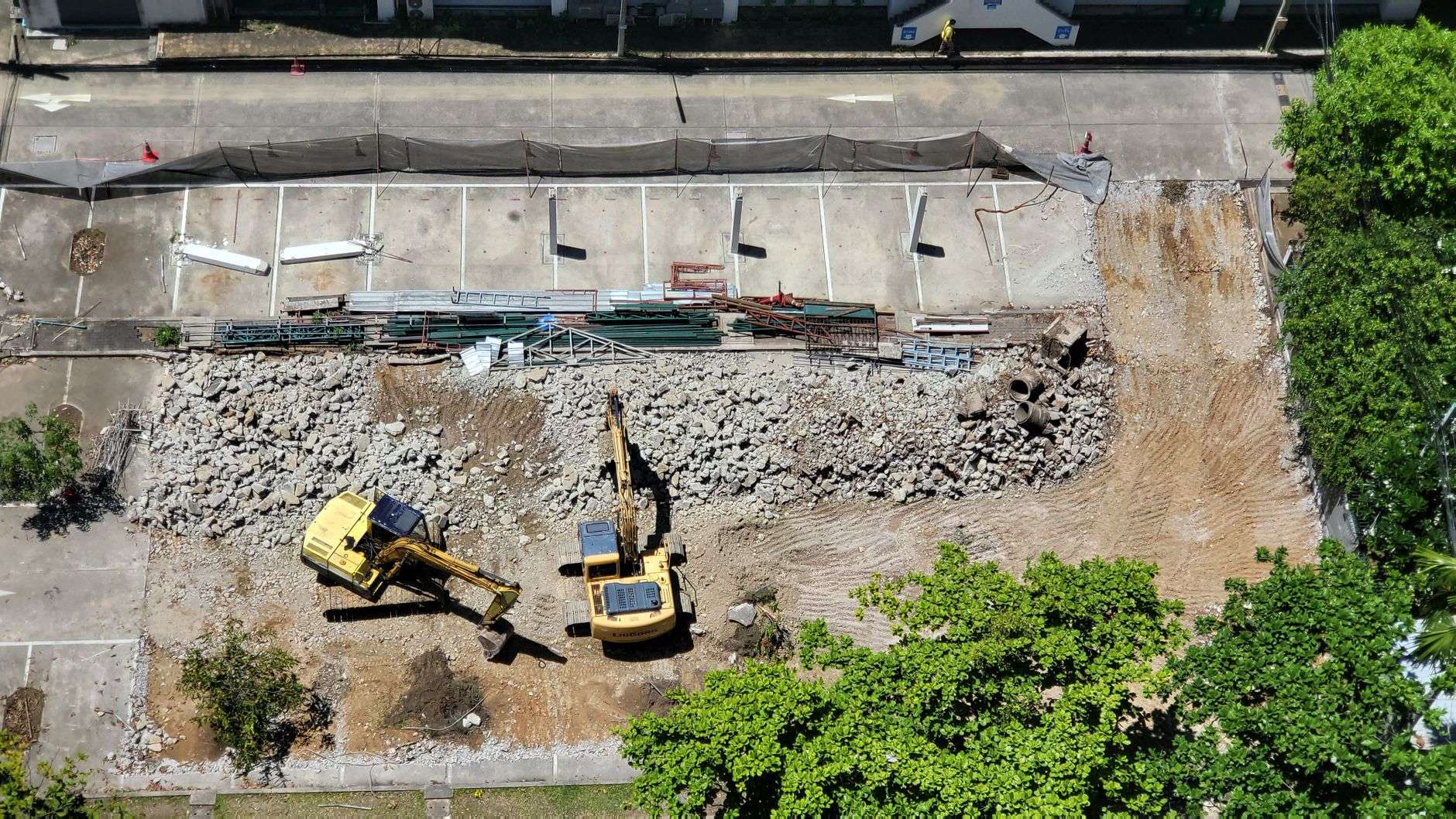 Aerial view of a commercial construction site with excavators clearing and grading a dirt lot next to a paved area