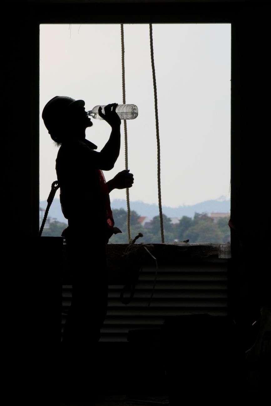Silhouette of a construction worker drinking from a water bottle at an outdoor building site