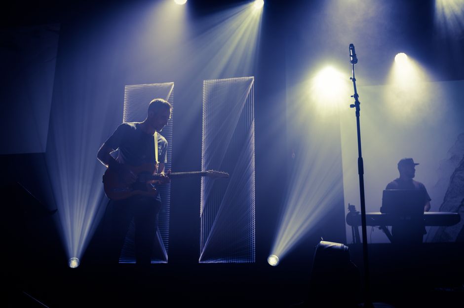 A guitarist performing live on a small club stage under warm lights