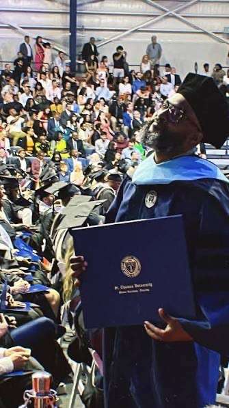 Courtney Bloom in academic regalia holding a diploma cover at a commencement ceremony