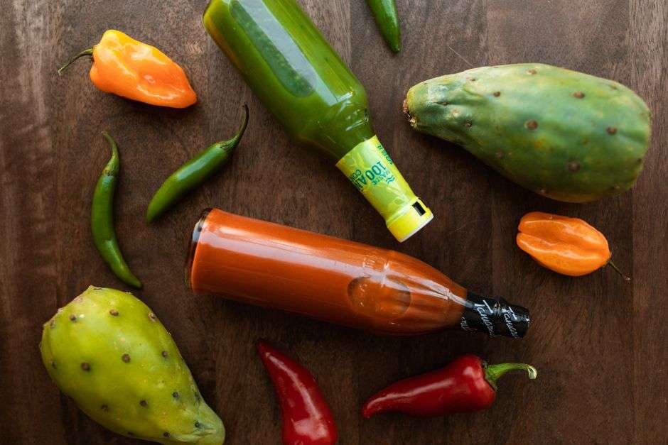 A bottle of cayenne pepper hot sauce beside fresh red chili peppers