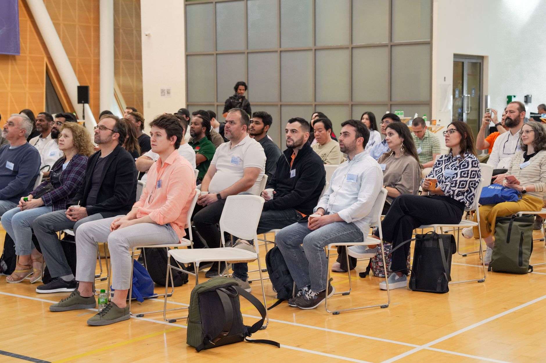 Rows of seated audience members facing a speaker at a community meeting in an auditorium