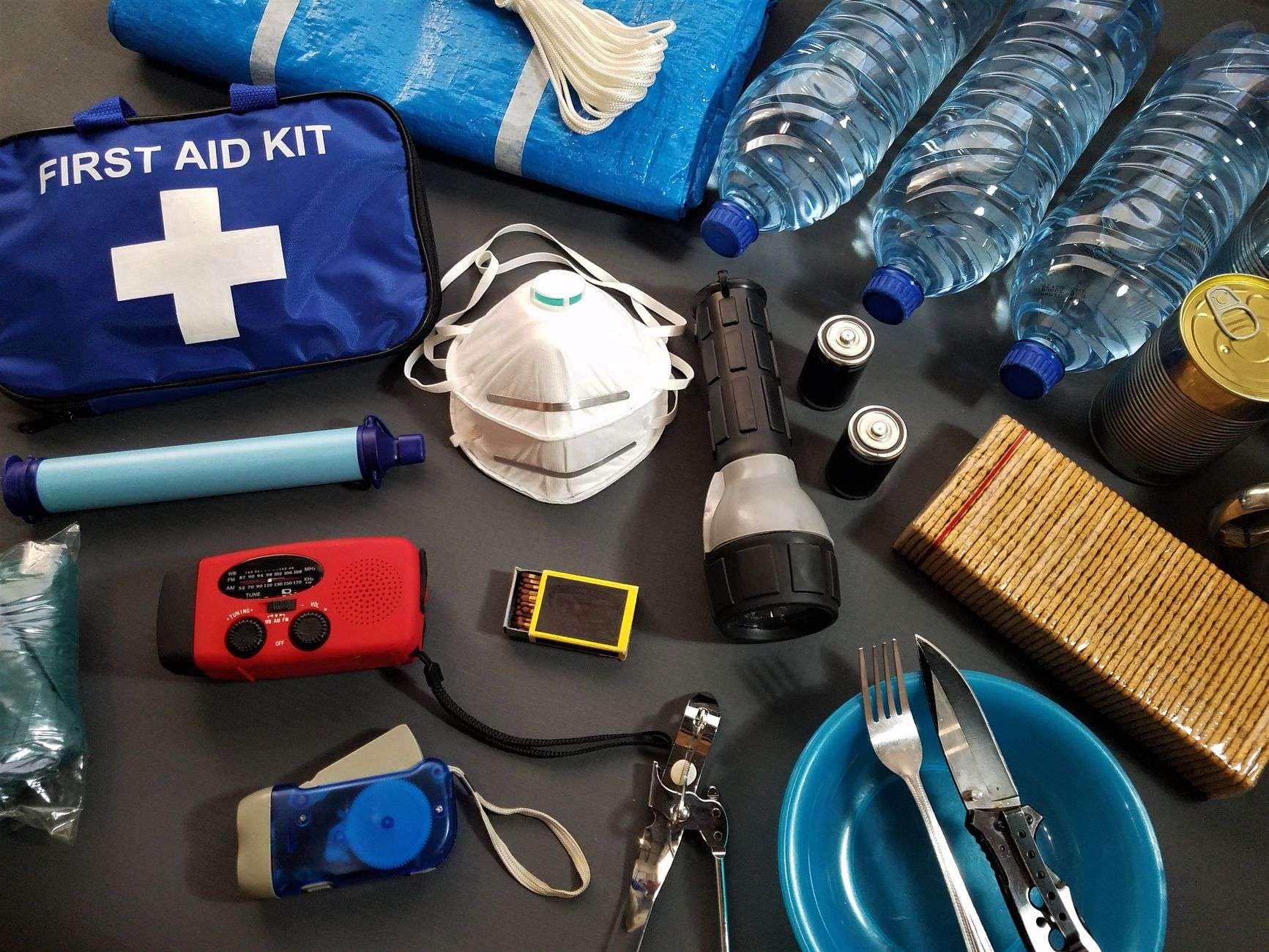 An emergency kit laid out with bottled water, a flashlight, batteries and first aid supplies
