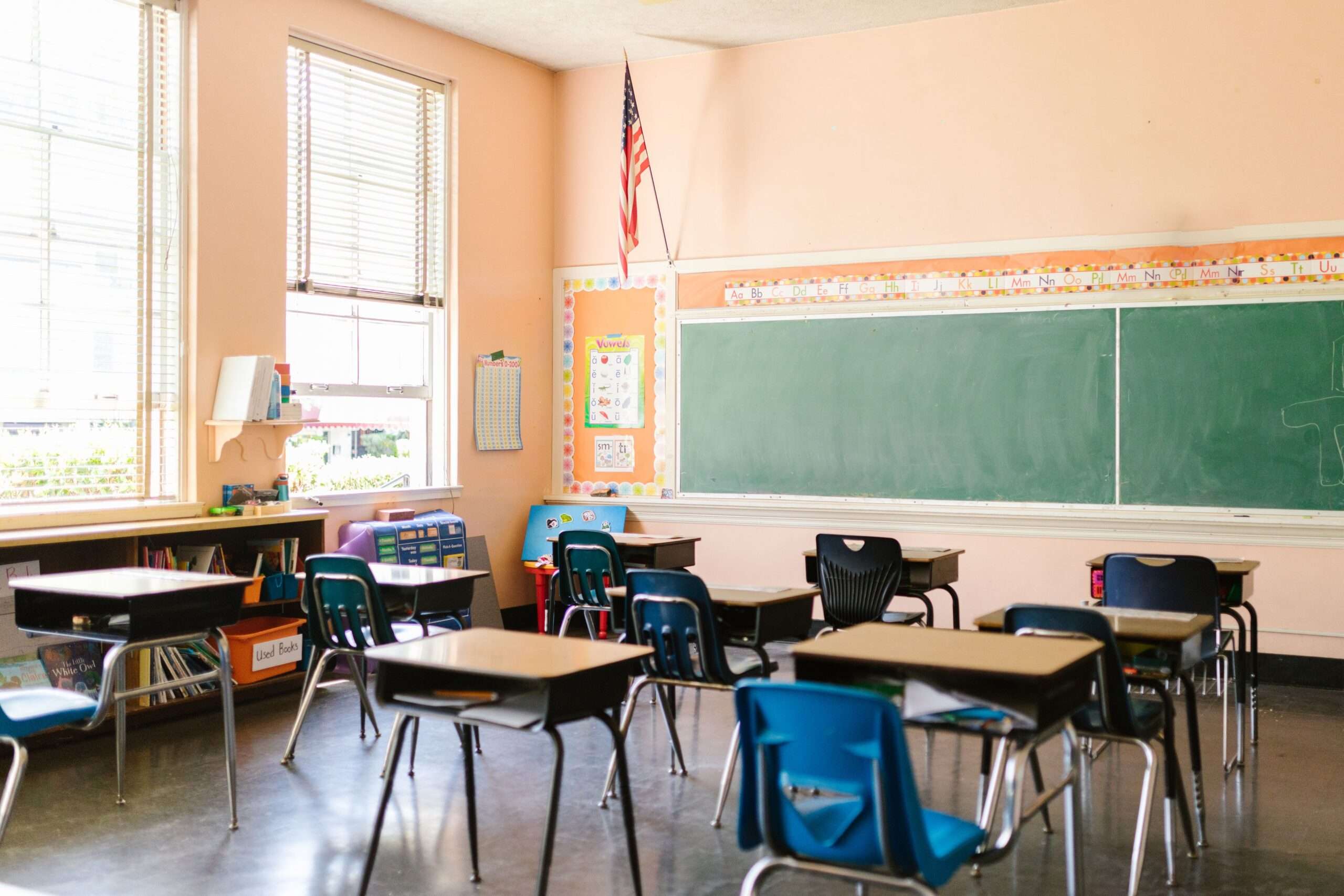Empty elementary school classroom with student desks, a chalkboard, and an American flag