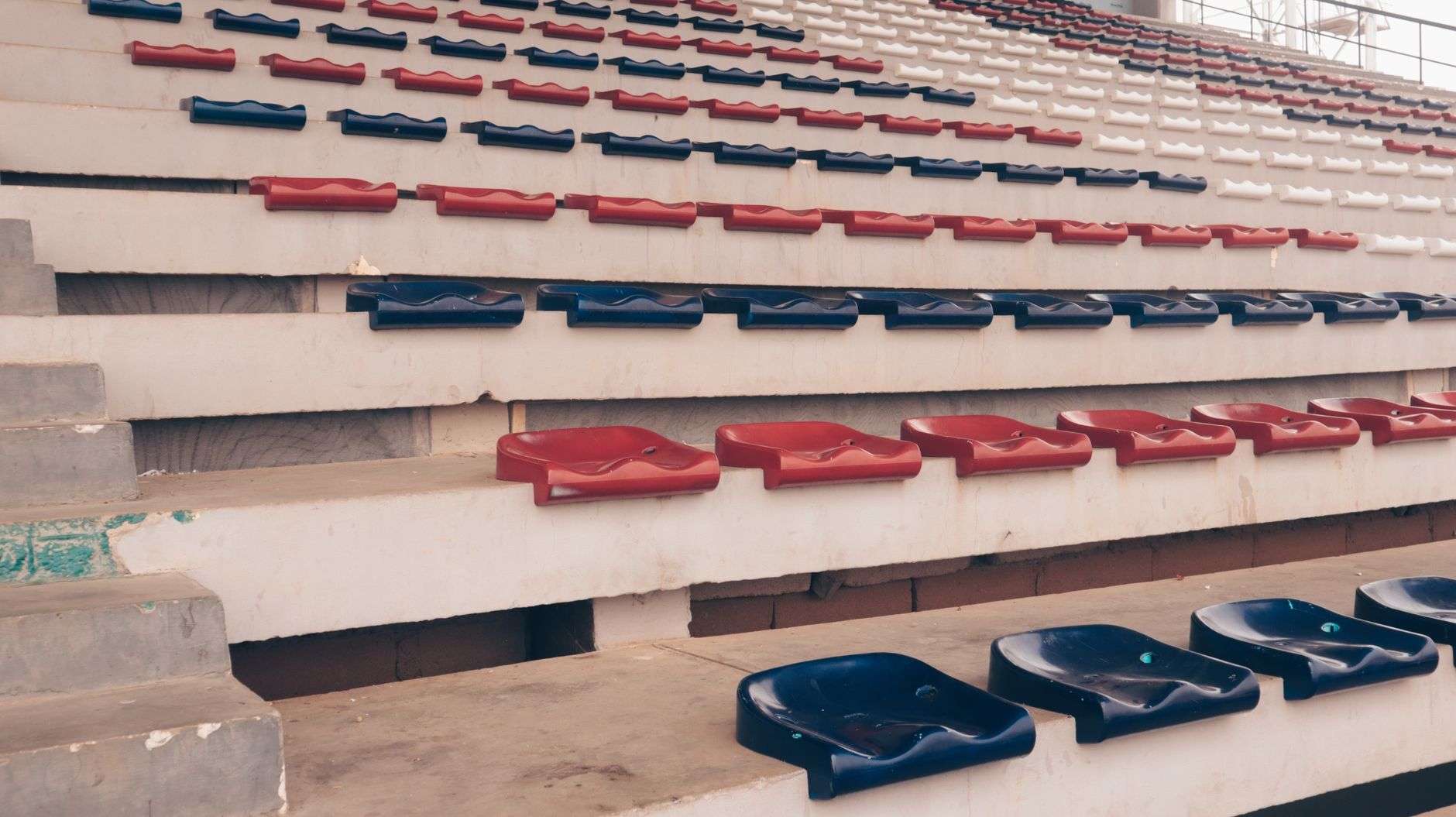 Empty stadium bleacher seating in red, blue, and white, with no event underway