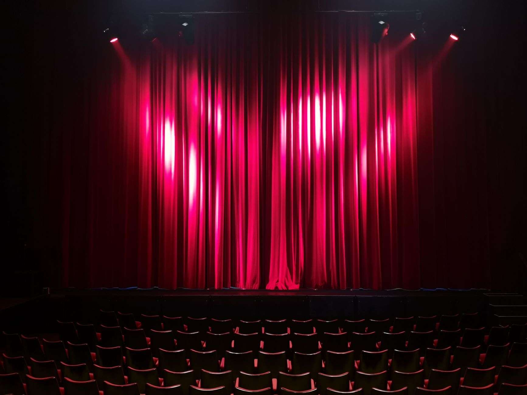 Empty theater stage with closed red curtains and rows of empty auditorium seating