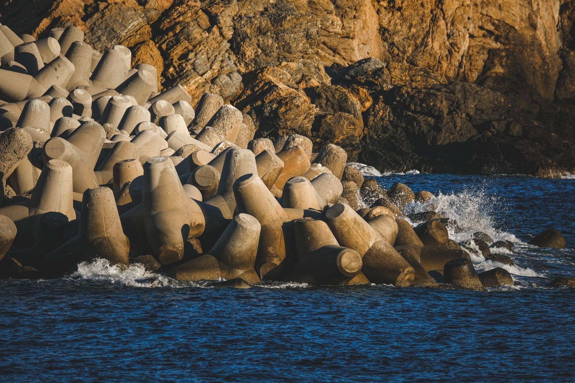 Stone breakwater structures sitting offshore in calm bay water near a sandy shoreline