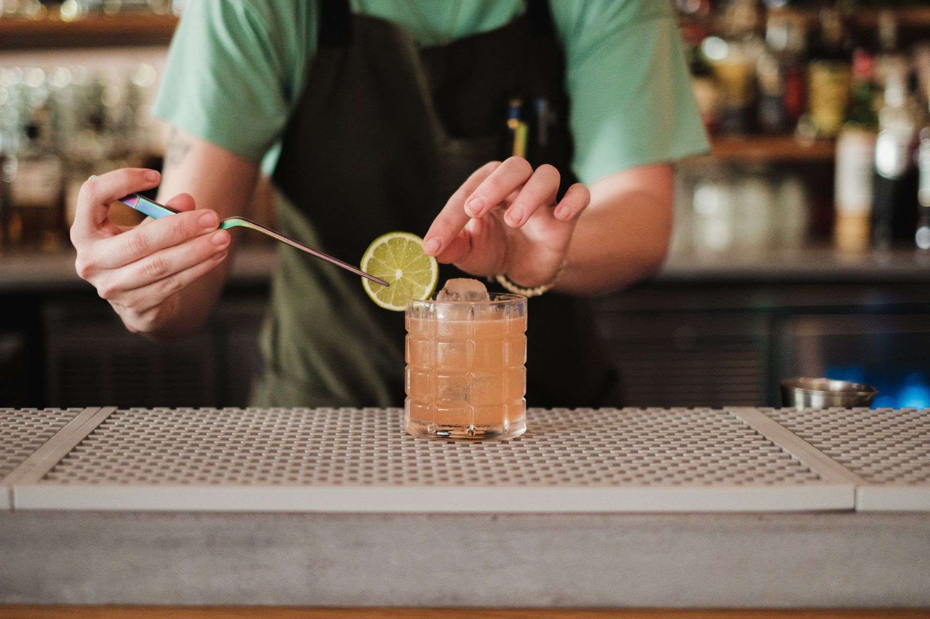 A bartender shaking and pouring a craft cocktail behind a bar