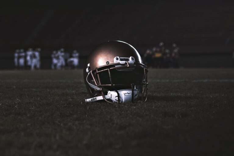 Football helmet resting on a grass field at night, with players blurred in the background