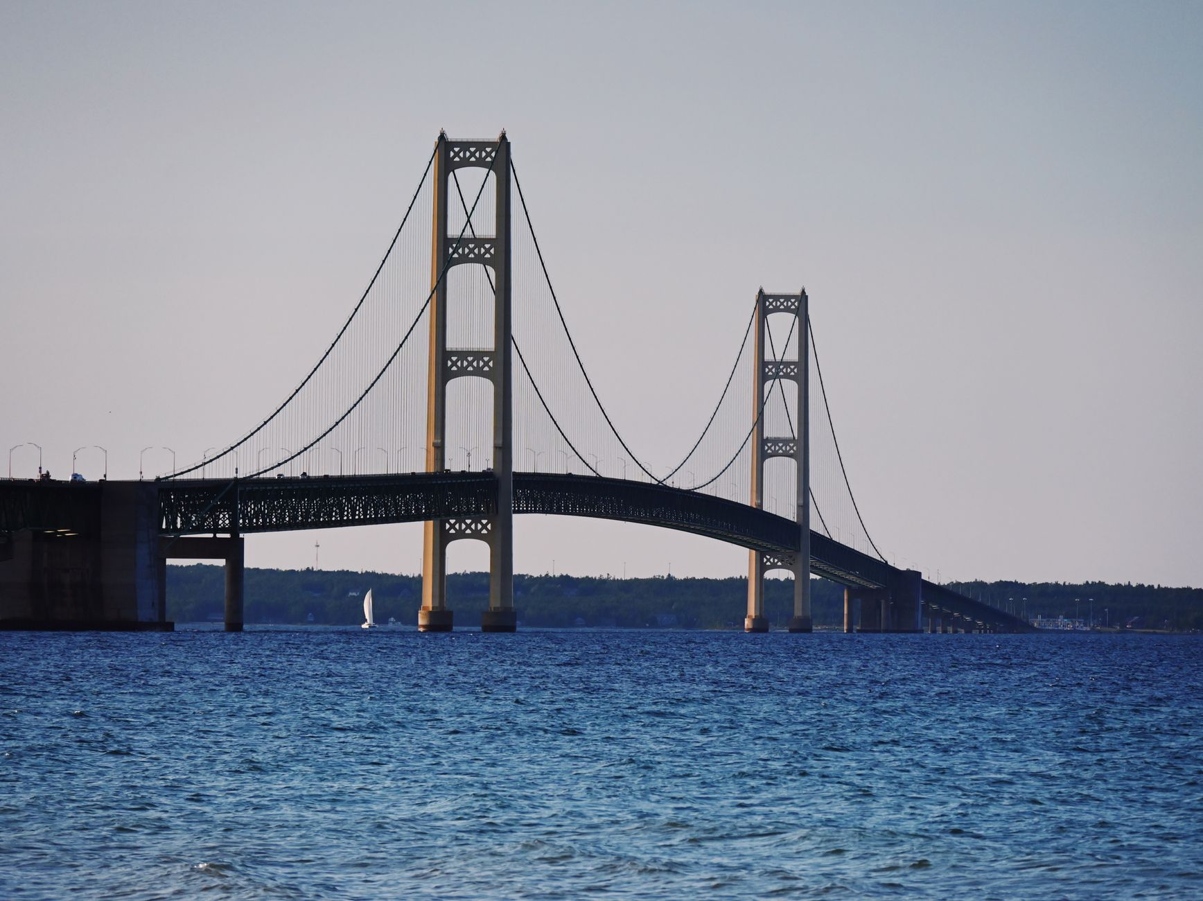 A long suspension bridge spans open water under a blue sky