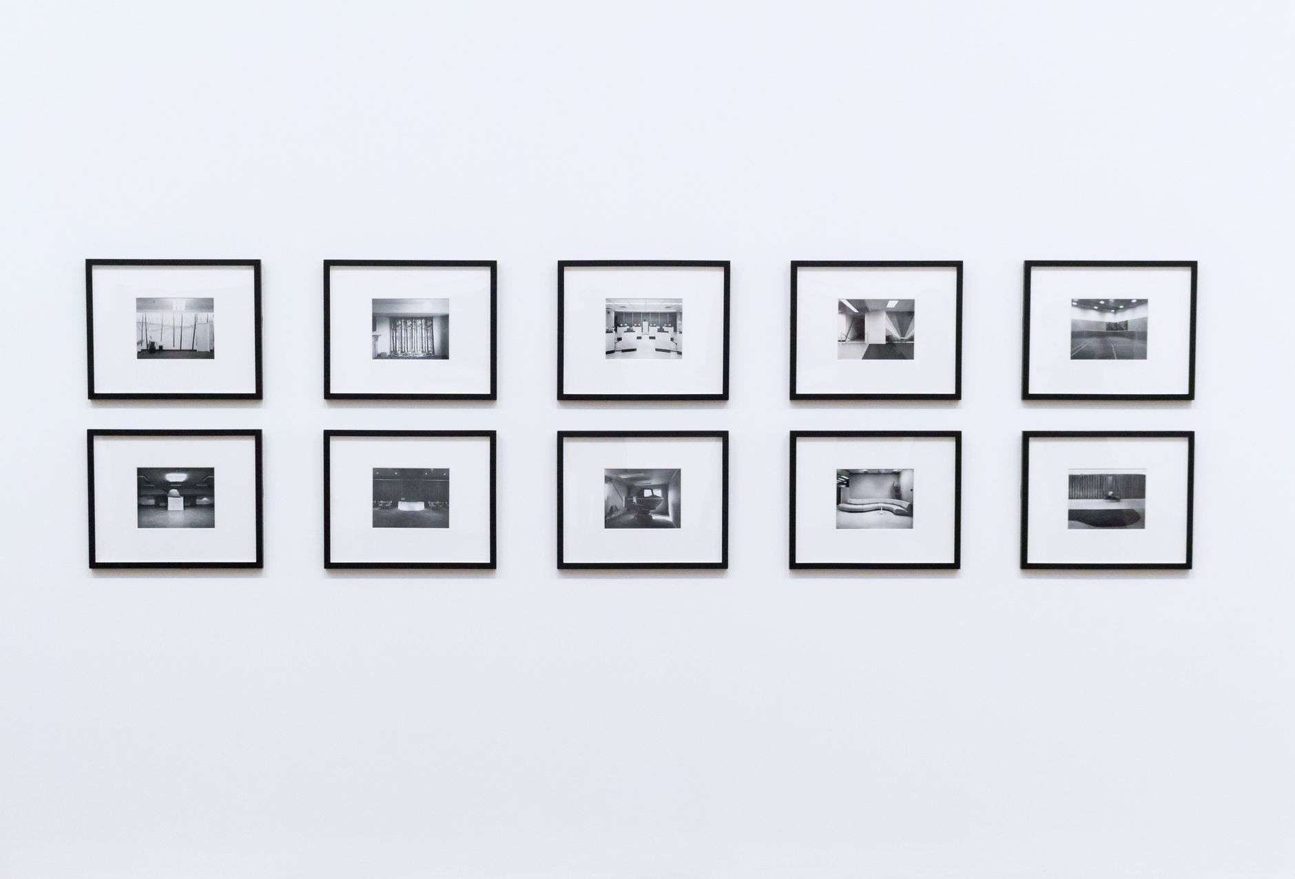 A row of small black-and-white framed photographs evenly spaced on a plain white gallery wall