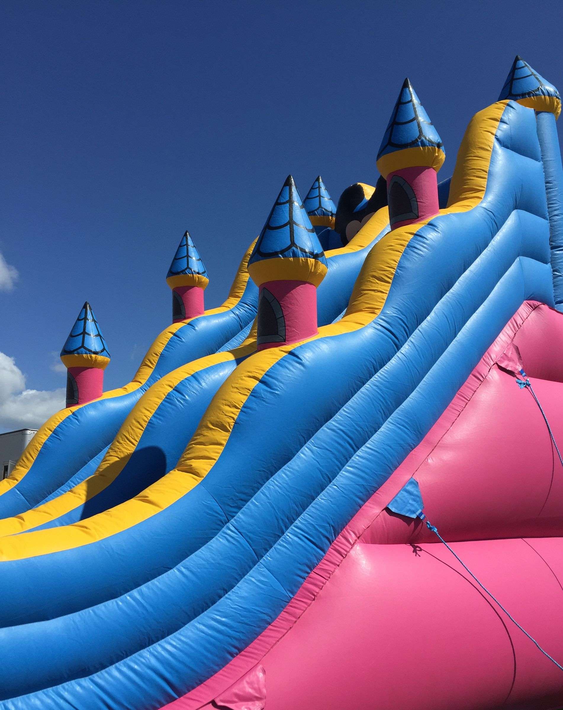 Bright multi-lane inflatable slide with colorful turrets set up outdoors under a clear blue sky