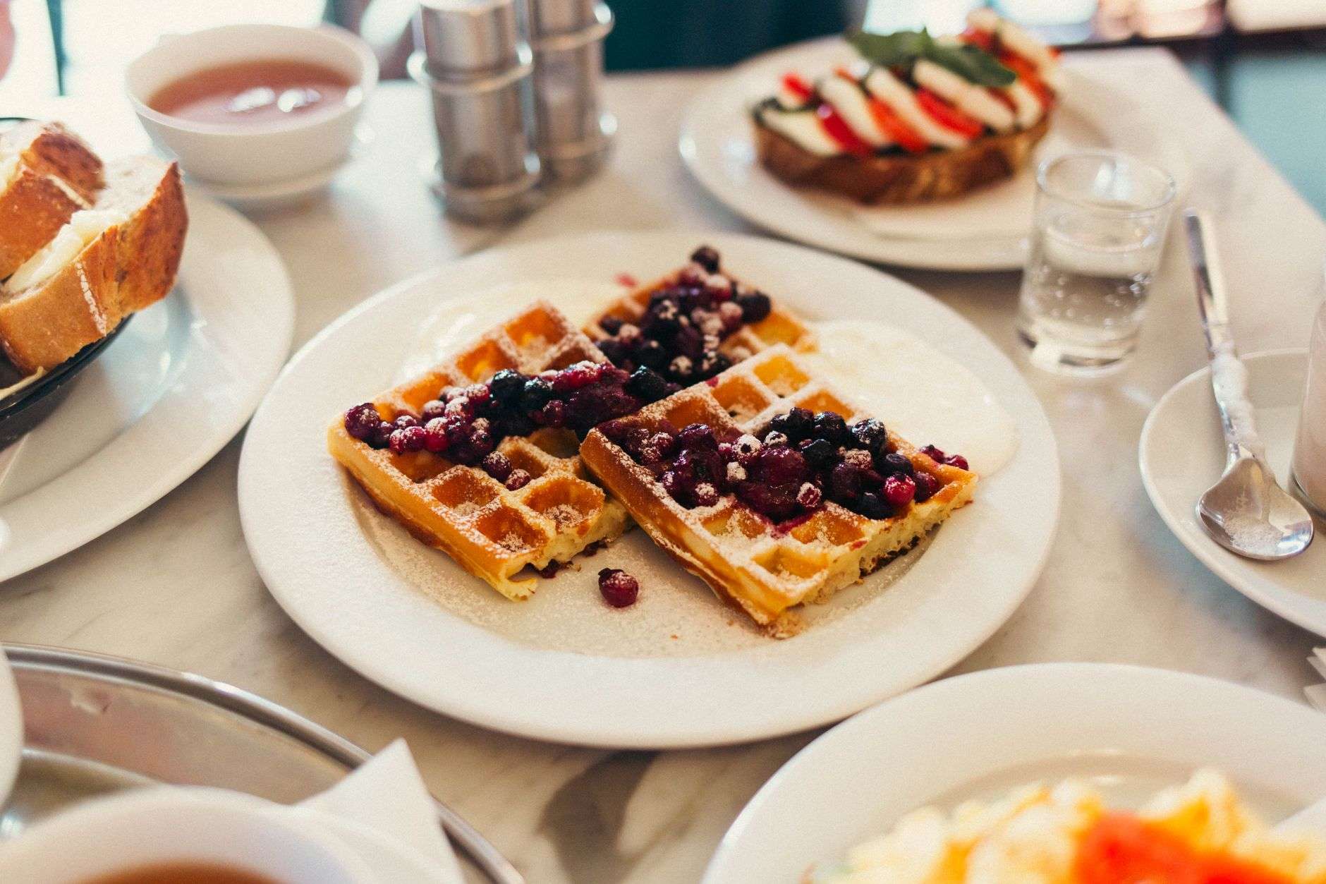 A plate of golden waffles topped with fruit and syrup on a restaurant table