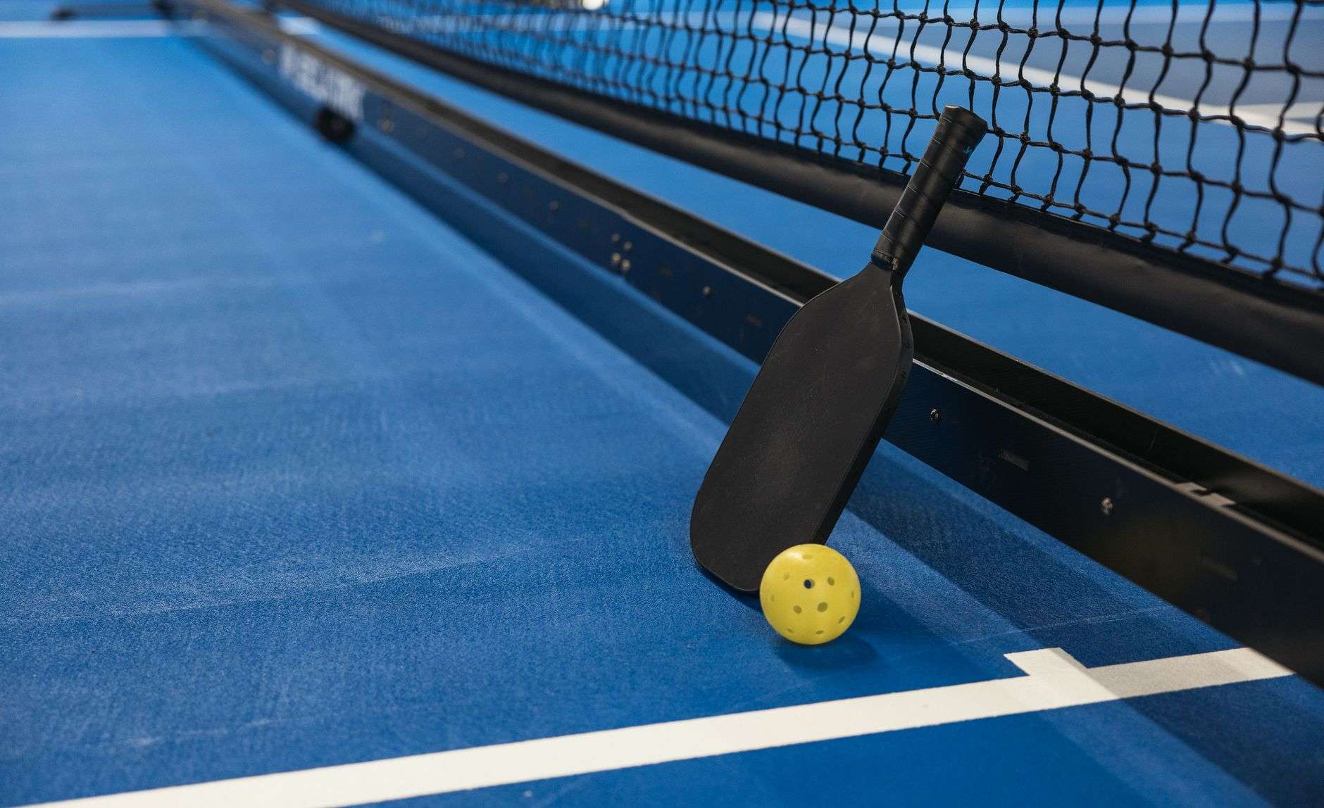 Pickleball paddles and a ball resting on an outdoor court