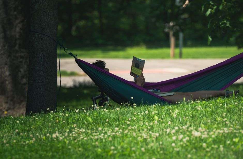 A stack of books beside a hammock ready for summer reading