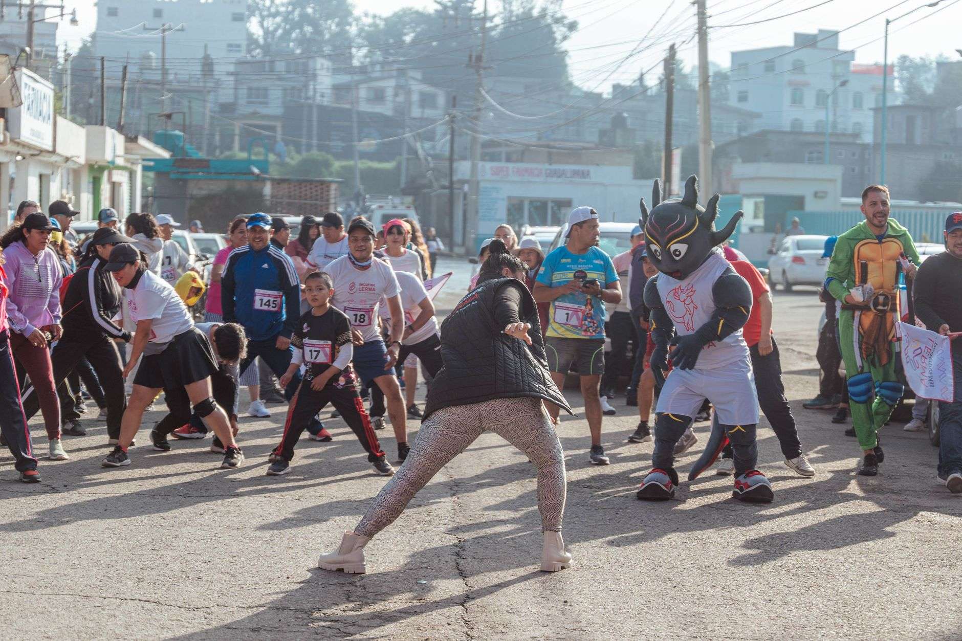 Runners with race bibs warming up on a street alongside a costumed mascot