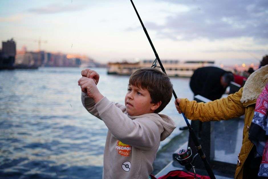 A child fishing with a rod from a wooden pier over the bay