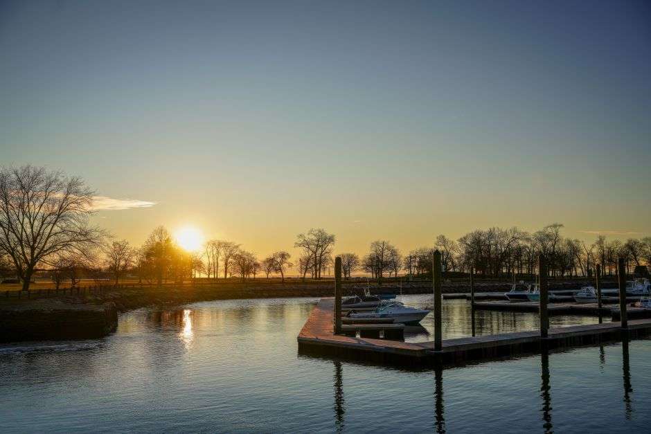 Boats tied up at a marina dock with sunset light on the water