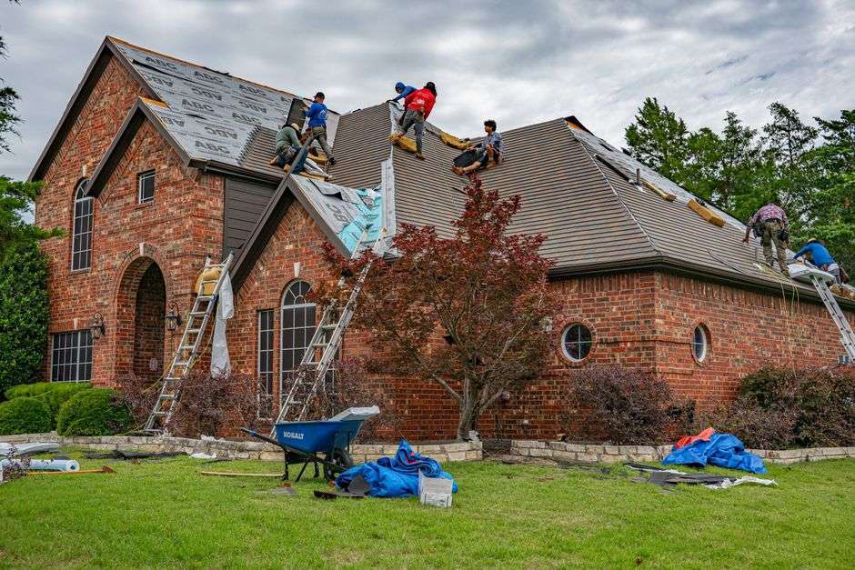 Construction workers installing shingles on the roof of a house