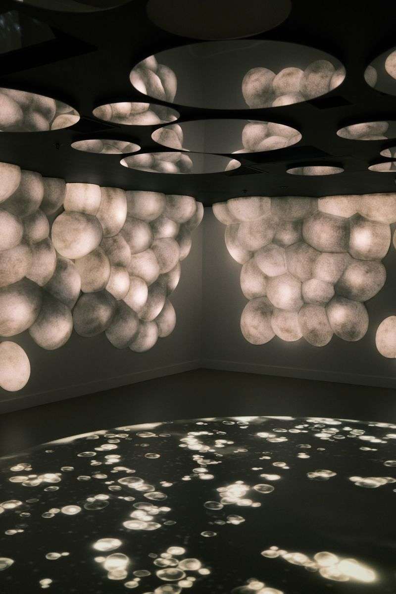 Immersive light art installation with glowing spherical projections covering a dark gallery ceiling and floor