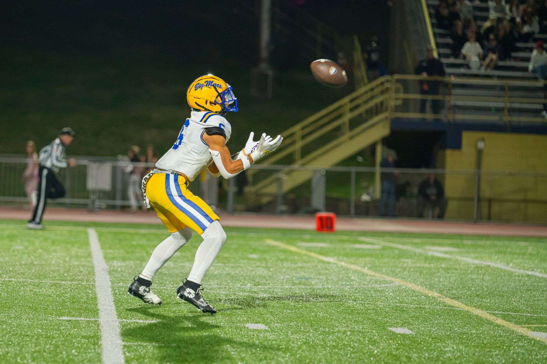 A football player reaching to catch a pass on a field at night