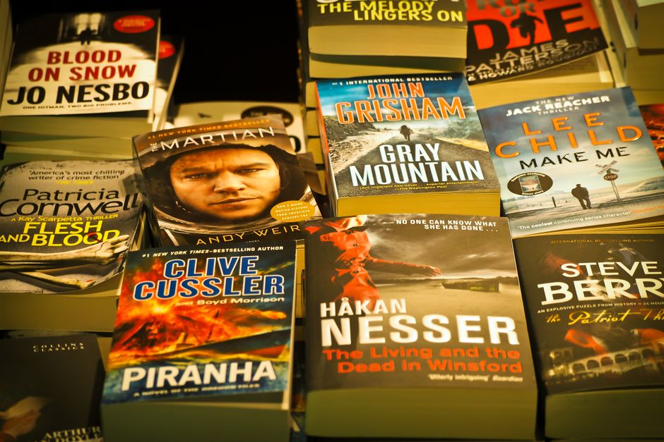 A paperback novel on a wooden railing with beach dunes in the background