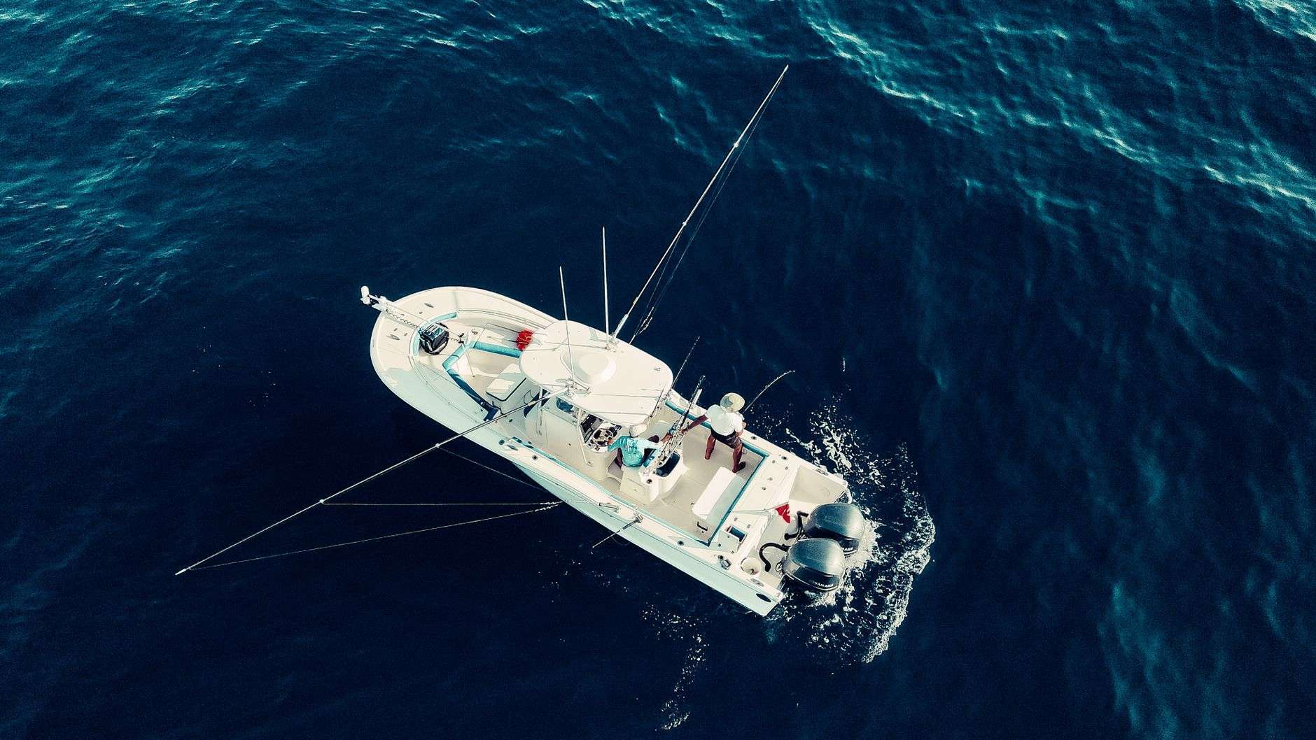 A sportfishing boat with outriggers cruises across open blue water