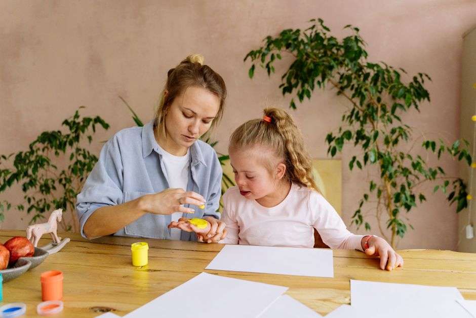 A caregiver reviewing paperwork at a kitchen table with a child nearby