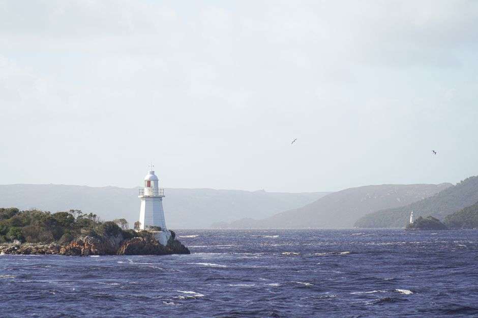 A lighthouse standing over calm bay water on a clear day