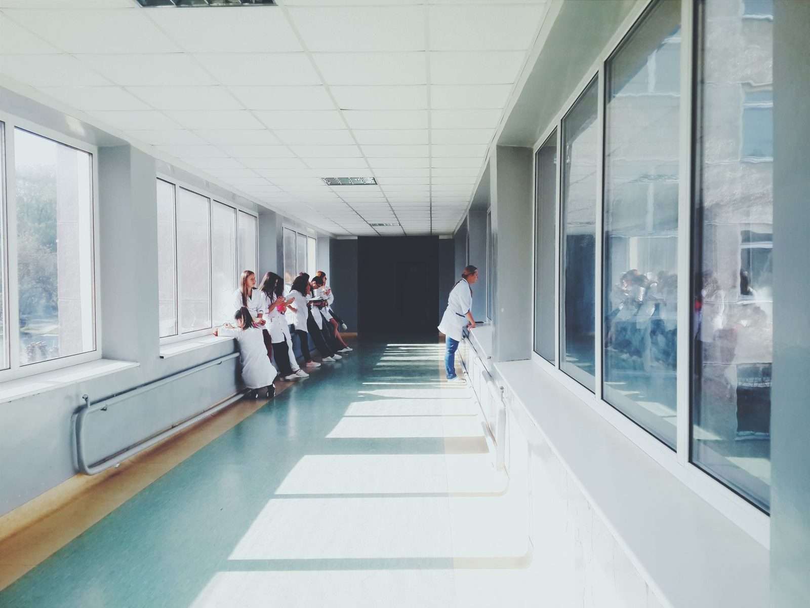 A sunlit hospital corridor with staff in white coats standing near large windows