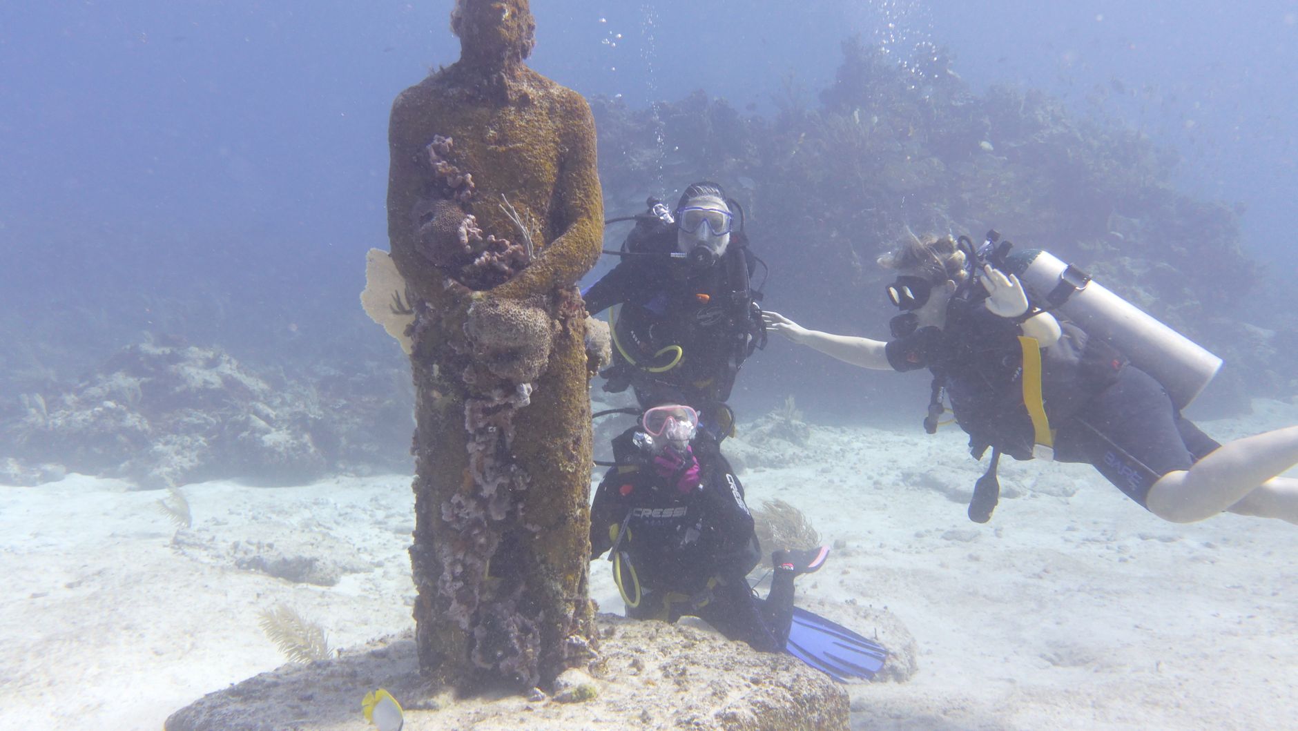 A diver swims near an underwater sculpture colonized by marine life