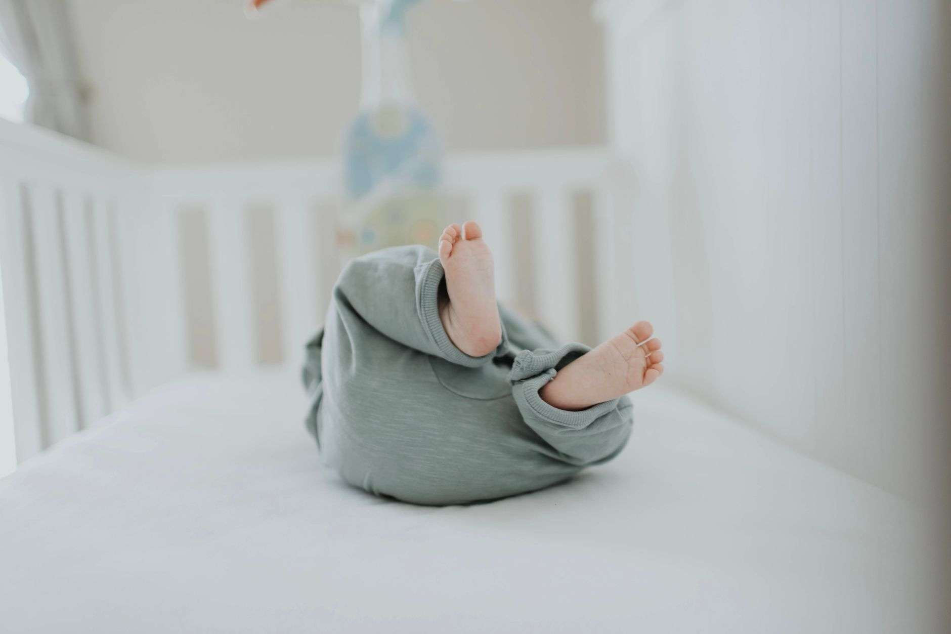 An empty crib with a firm mattress and fitted sheet and no pillows, blankets or toys