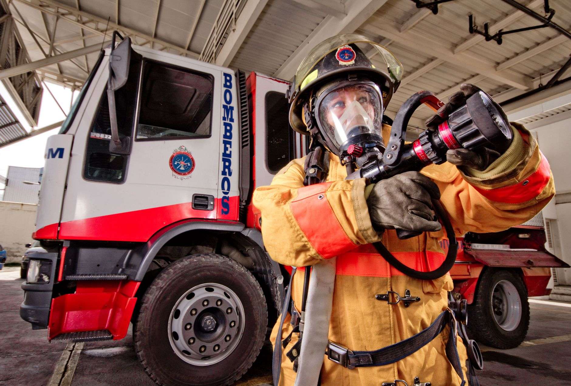 A firefighter in turnout gear standing beside a fire engine inside a station bay