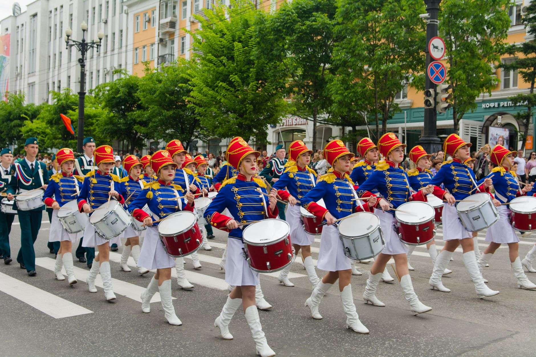 A marching band in uniform performing along a downtown parade route lined with spectators