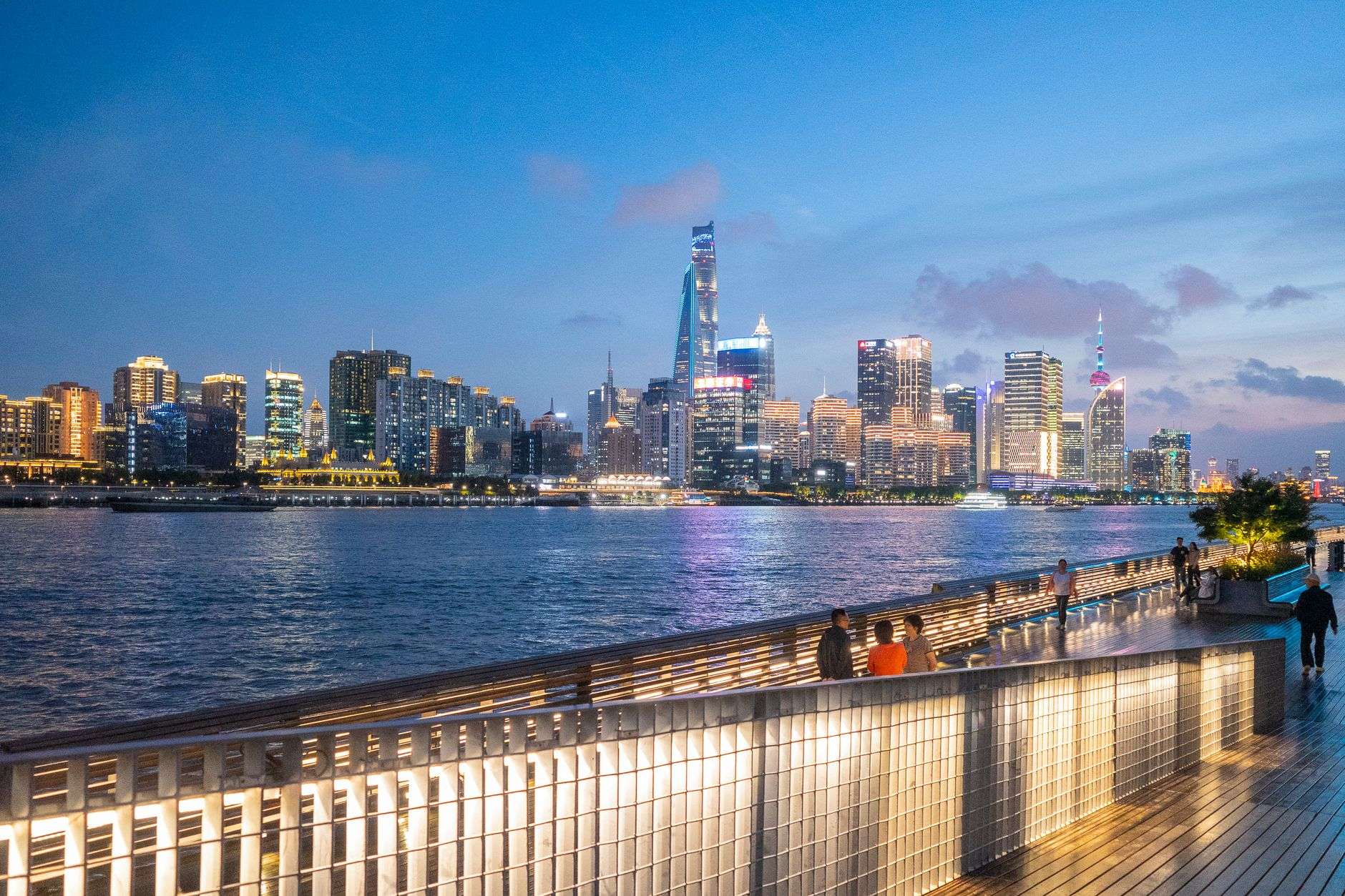 A pedestrian promenade running alongside an urban waterfront with walking paths and greenery
