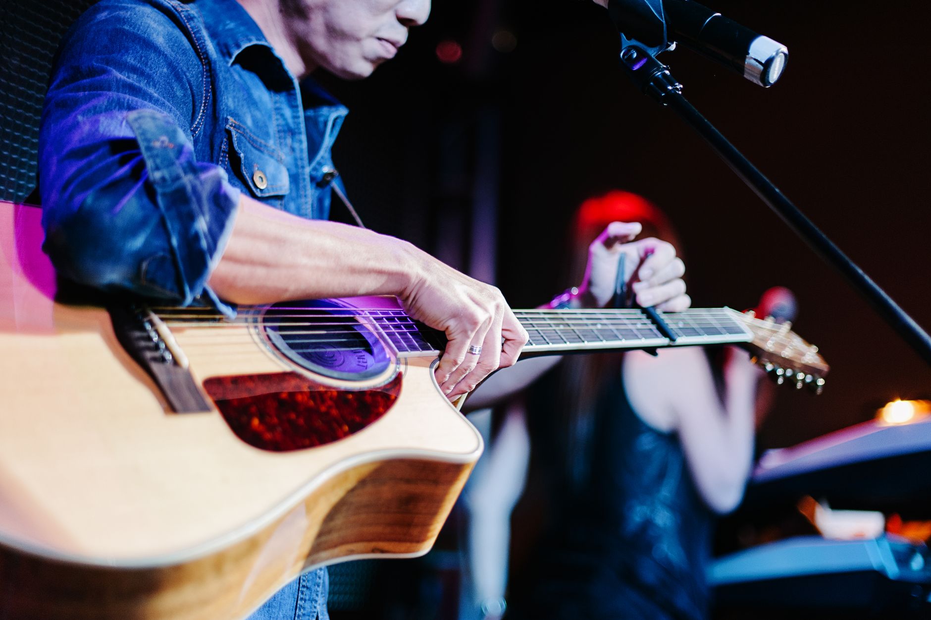 Musician playing an acoustic guitar on a small stage under warm lights